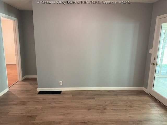 unfurnished room featuring baseboards, wood finished floors, and visible vents