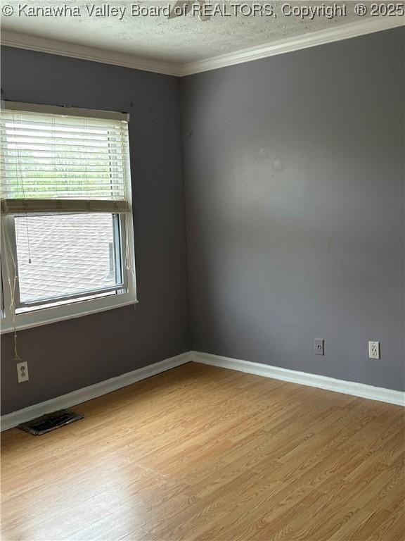 spare room with baseboards, ornamental molding, wood finished floors, and visible vents