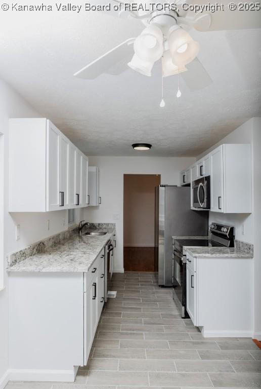 kitchen with ceiling fan, appliances with stainless steel finishes, a sink, white cabinetry, and baseboards