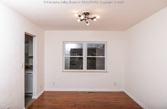 spare room with a notable chandelier, baseboards, visible vents, and wood finished floors