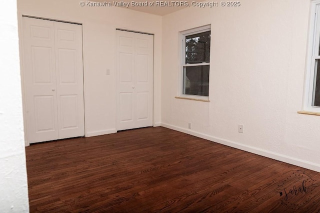 unfurnished bedroom with two closets, baseboards, and dark wood finished floors