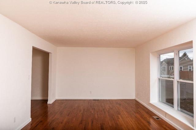 empty room with baseboards, wood finished floors, and visible vents