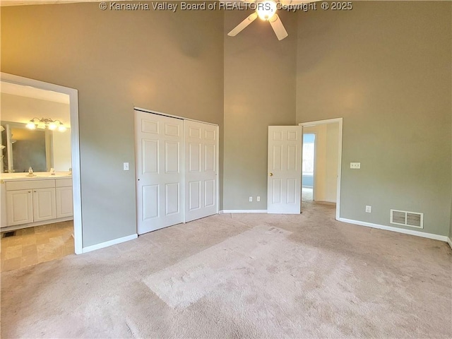 unfurnished bedroom with light carpet, a sink, baseboards, a towering ceiling, and visible vents