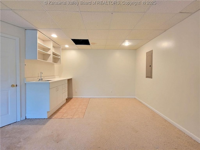 interior space with open shelves, light carpet, a sink, a paneled ceiling, and electric panel