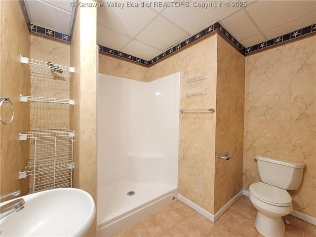 bathroom featuring toilet, a drop ceiling, a walk in shower, tile patterned floors, and a sink