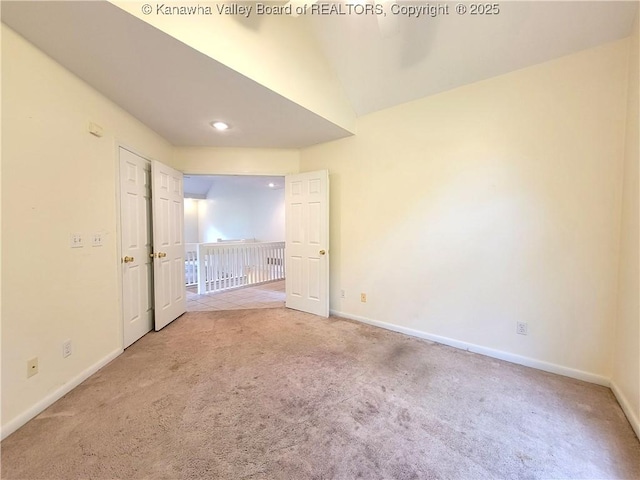 carpeted spare room featuring baseboards and lofted ceiling