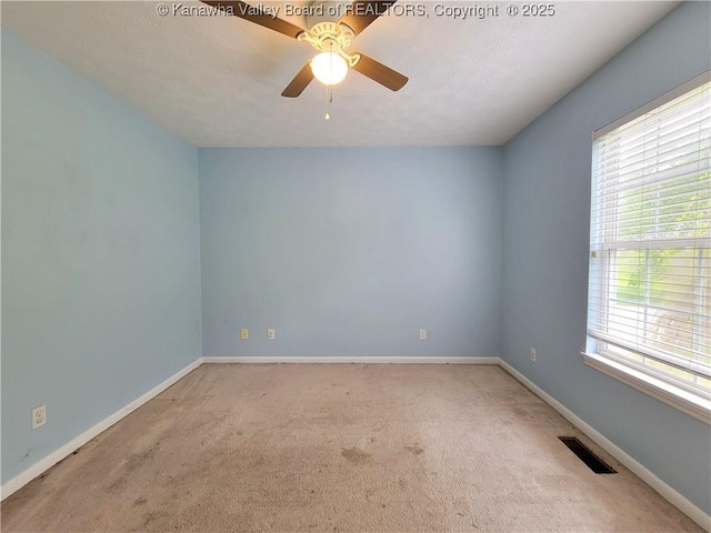 carpeted empty room with ceiling fan, baseboards, visible vents, and a wealth of natural light