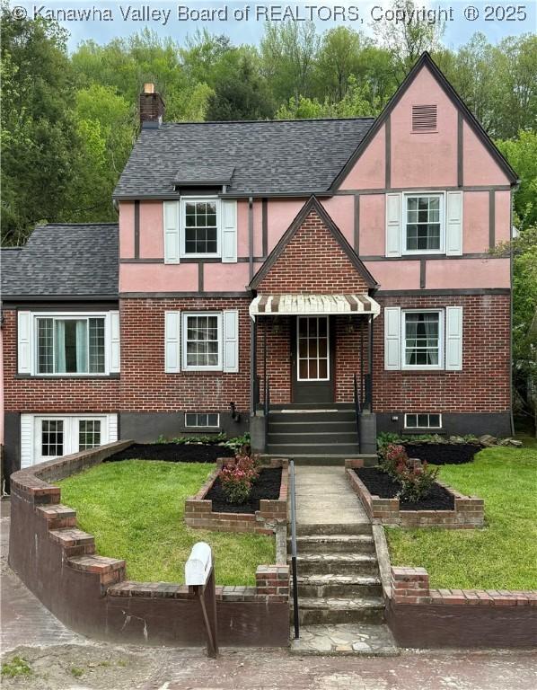 english style home featuring a shingled roof, a front lawn, stucco siding, and a chimney
