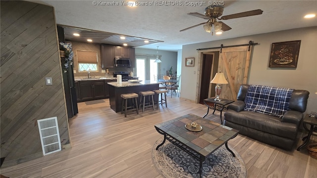 living room featuring ceiling fan, a barn door, a textured ceiling, light wood-type flooring, and visible vents