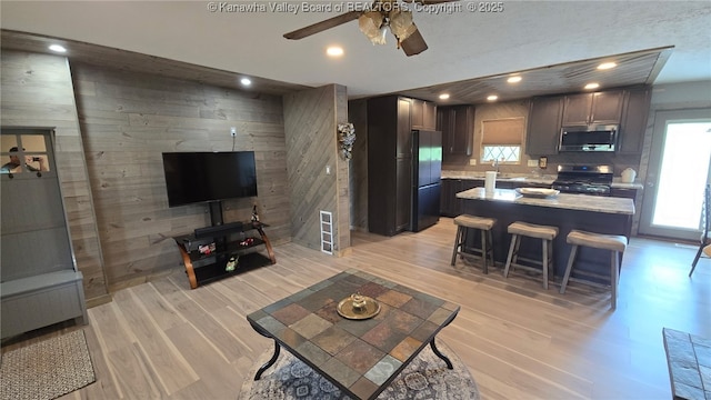 living room with wooden walls, a ceiling fan, recessed lighting, and light wood-style flooring