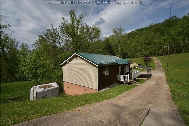 view of home's exterior with a porch, crawl space, a view of trees, a yard, and metal roof