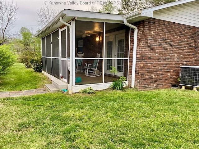 view of home's exterior featuring a lawn, french doors, brick siding, a sunroom, and central AC unit