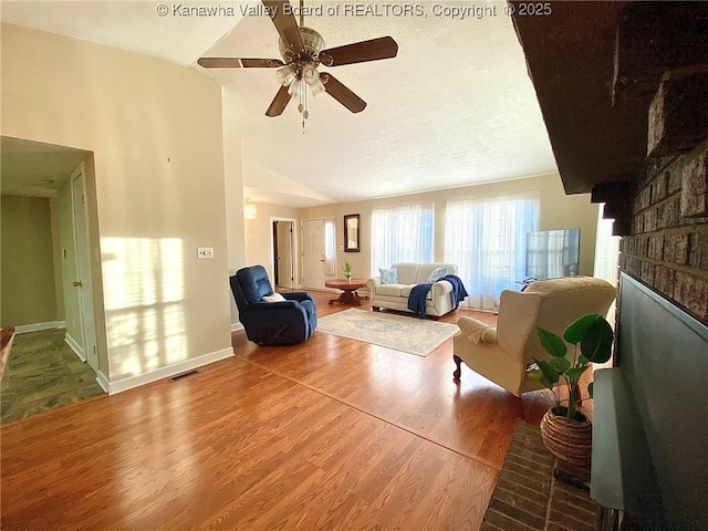 living area featuring wood finished floors, a fireplace, visible vents, ceiling fan, and lofted ceiling