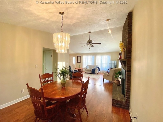 dining space featuring baseboards, ceiling fan with notable chandelier, a textured ceiling, and wood finished floors