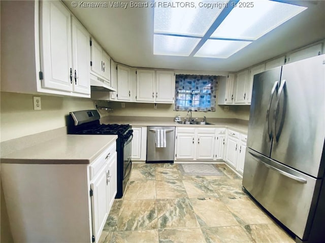 kitchen featuring stone finish flooring, a sink, white cabinetry, light countertops, and appliances with stainless steel finishes