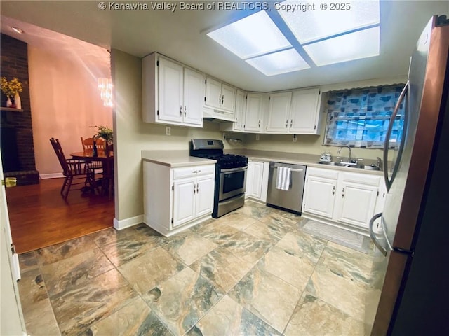 kitchen with a sink, stainless steel appliances, under cabinet range hood, white cabinets, and baseboards