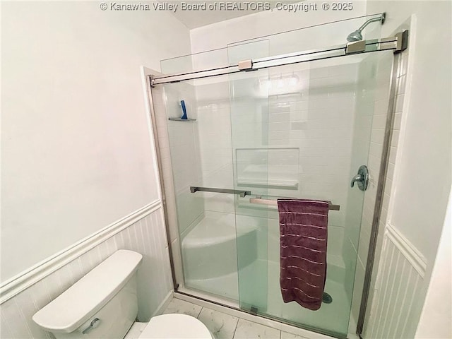 full bath featuring a wainscoted wall, toilet, a decorative wall, and a stall shower