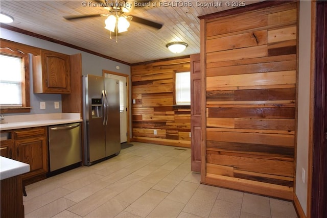 kitchen featuring brown cabinets, ceiling fan, light countertops, appliances with stainless steel finishes, and wooden walls