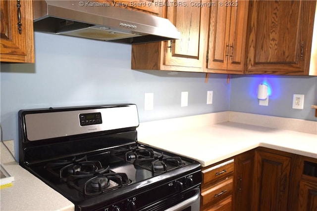 kitchen featuring stainless steel gas range, light countertops, brown cabinetry, and under cabinet range hood