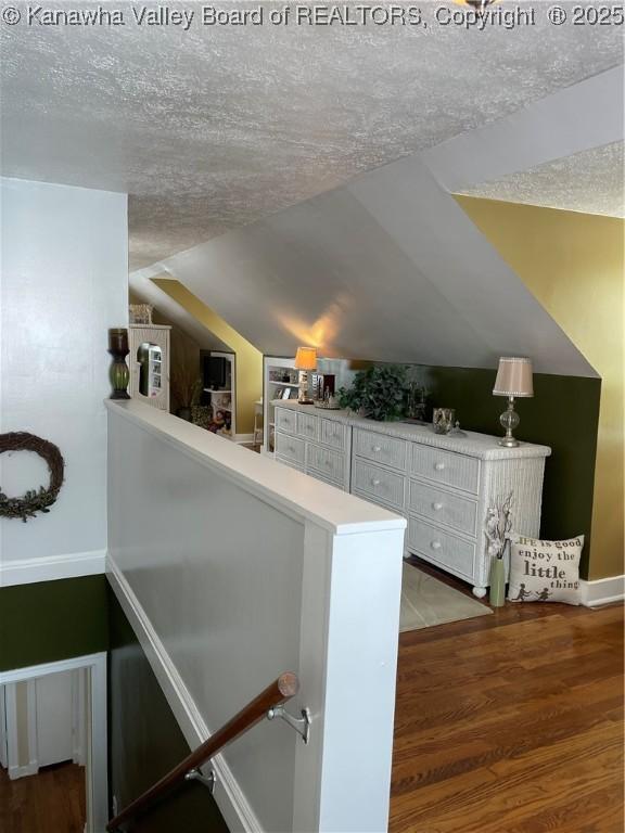 interior space featuring lofted ceiling, baseboards, a textured ceiling, and wood finished floors