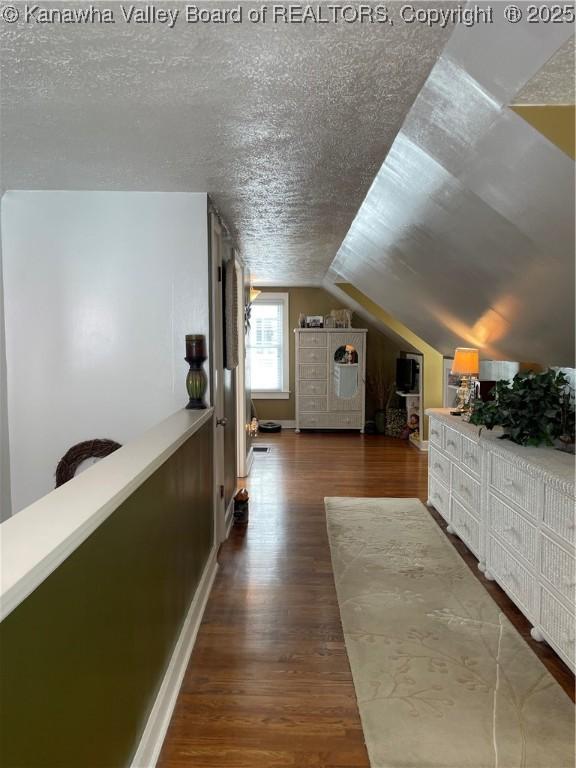 additional living space with vaulted ceiling, a textured ceiling, baseboards, and wood finished floors
