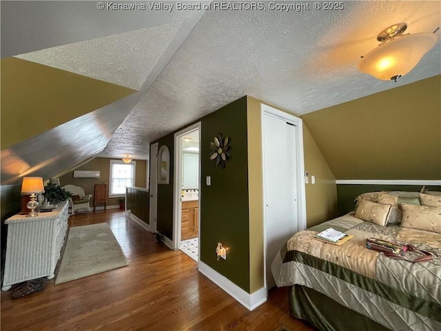 bedroom featuring lofted ceiling, wood finished floors, a textured ceiling, ensuite bath, and baseboards