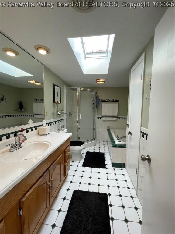 full bath with a skylight, vanity, tiled bath, a stall shower, and tile patterned floors