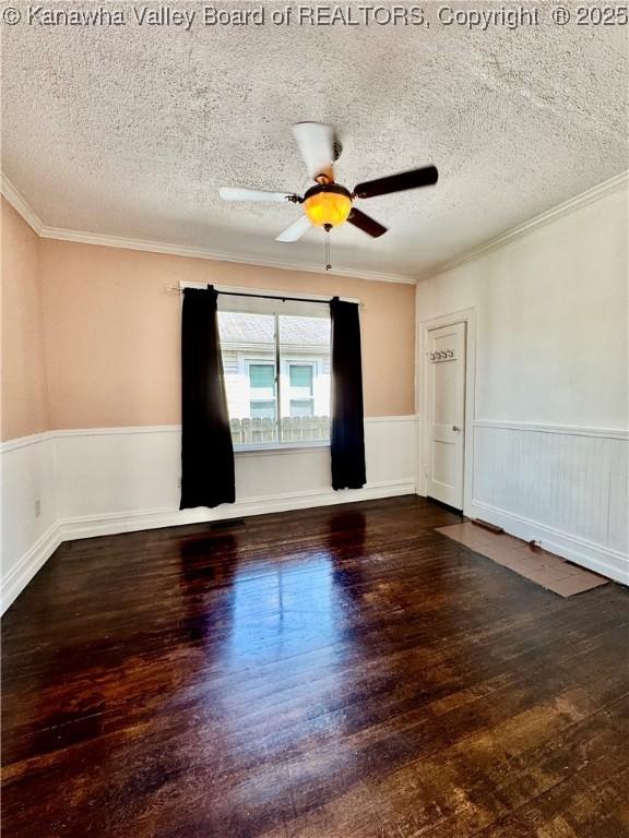 spare room featuring a textured ceiling, hardwood / wood-style floors, crown molding, and a wainscoted wall