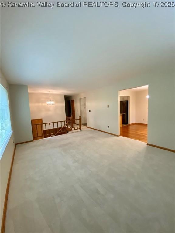unfurnished living room featuring carpet flooring, an inviting chandelier, and baseboards