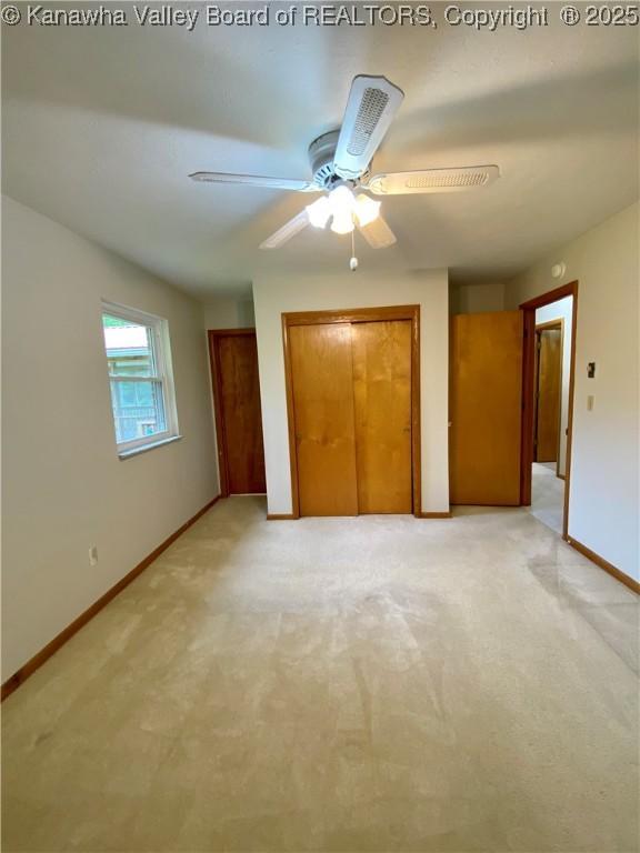 unfurnished bedroom with light colored carpet, two closets, baseboards, and ceiling fan