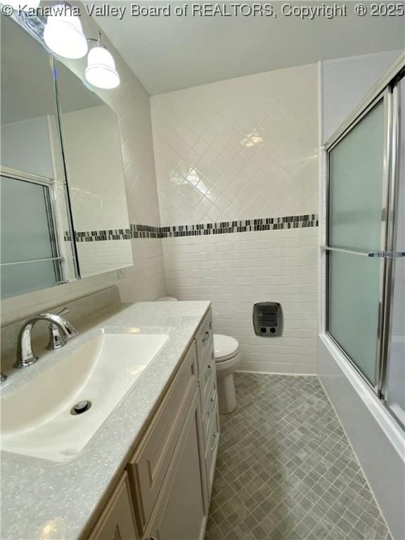 bathroom with toilet, tile walls, vanity, and enclosed tub / shower combo