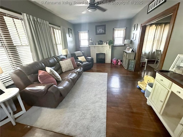 living room with a ceiling fan, dark wood-type flooring, and a brick fireplace
