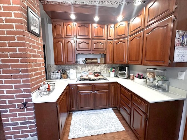 kitchen featuring stainless steel stovetop, light countertops, light wood-type flooring, brown cabinetry, and decorative backsplash