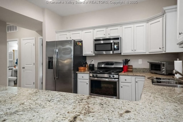 kitchen featuring stainless steel appliances, white cabinetry, a sink, and light stone counters