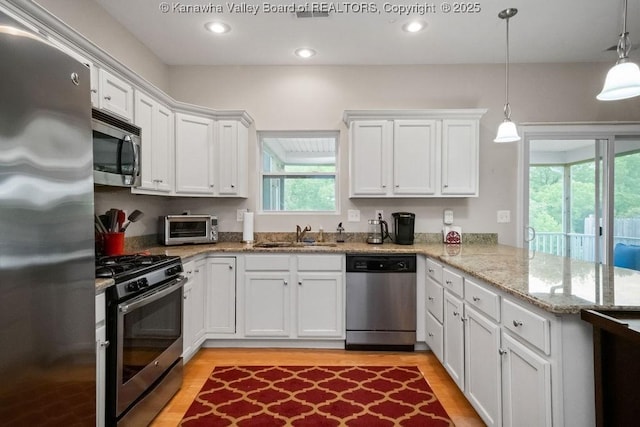 kitchen with stainless steel appliances, a sink, a peninsula, white cabinetry, and light wood-type flooring