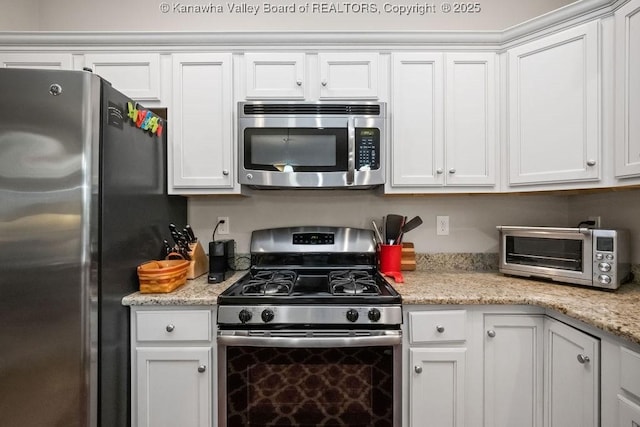 kitchen with stainless steel appliances, white cabinets, and light stone countertops