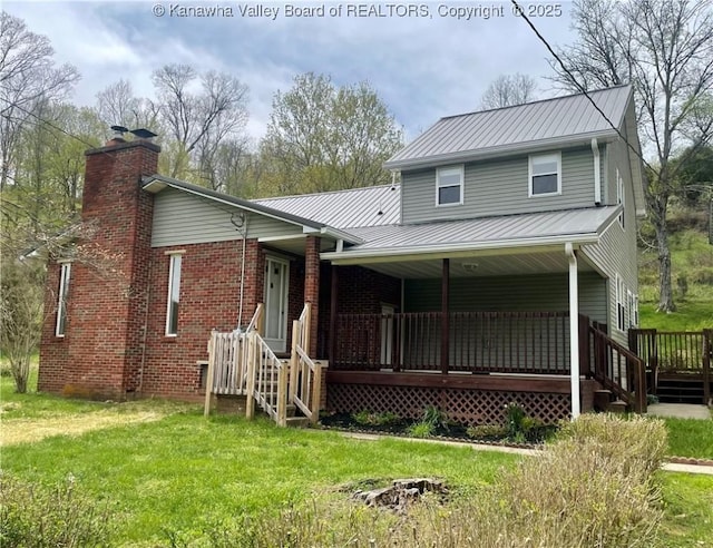 view of front of house with a front lawn, metal roof, a porch, a chimney, and brick siding