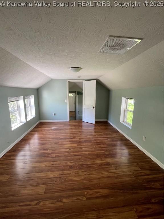 additional living space featuring lofted ceiling, dark wood-style floors, a textured ceiling, and baseboards