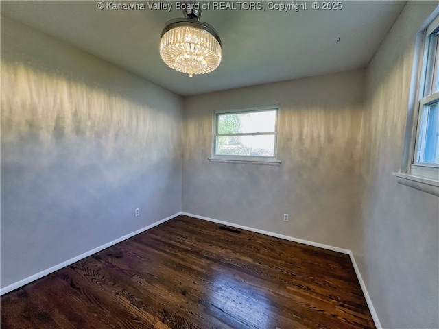 empty room with a chandelier, wood finished floors, and baseboards