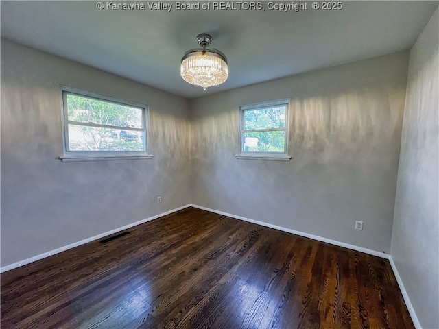 empty room featuring wood finished floors, a chandelier, and baseboards