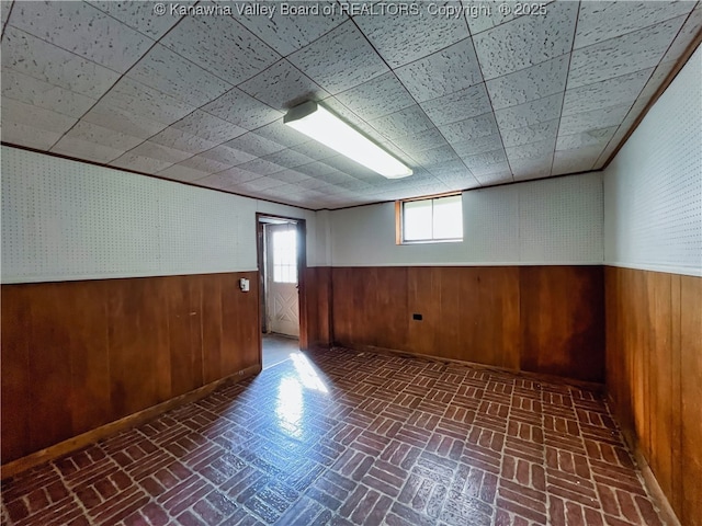 below grade area with wooden walls, wainscoting, and brick patterned floors