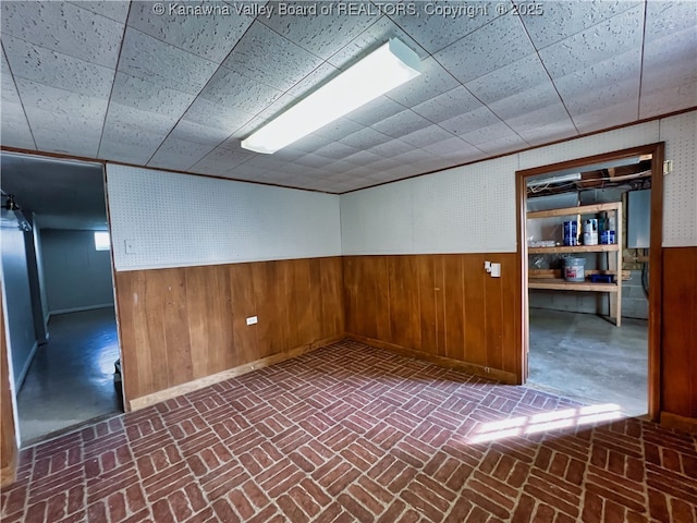 unfurnished room featuring wooden walls, brick floors, and a wainscoted wall