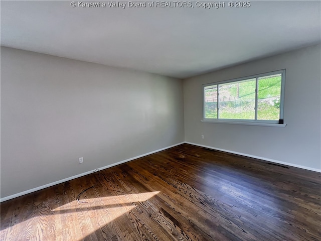 spare room with baseboards and dark wood-style flooring