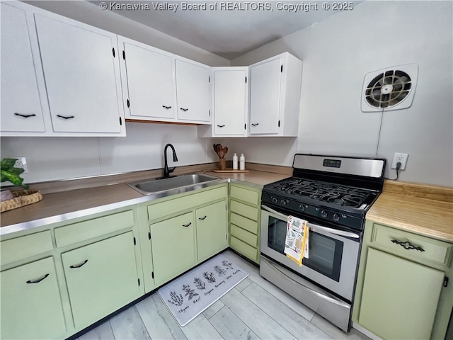 kitchen with gas range, a sink, white cabinetry, and light wood-type flooring