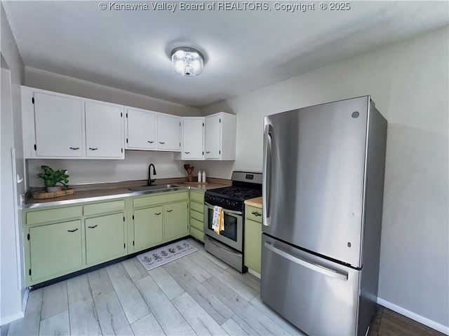 kitchen featuring stainless steel appliances, a sink, light wood finished floors, green cabinets, and white cabinets