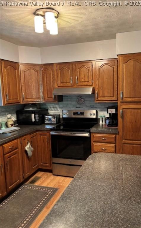 5222 Dalewood Dr, Charleston, WV 25313 - kitchen featuring stainless steel electric stove, dark countertops, under cabinet range hood, and brown cabinets