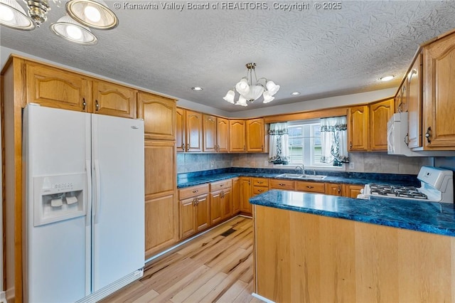 kitchen featuring white appliances, a chandelier, a sink, dark countertops, and light wood-type flooring