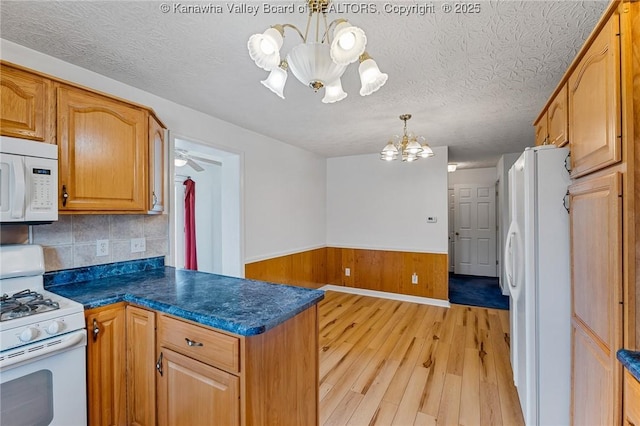 kitchen with white appliances, a chandelier, light wood-style floors, dark countertops, and a peninsula