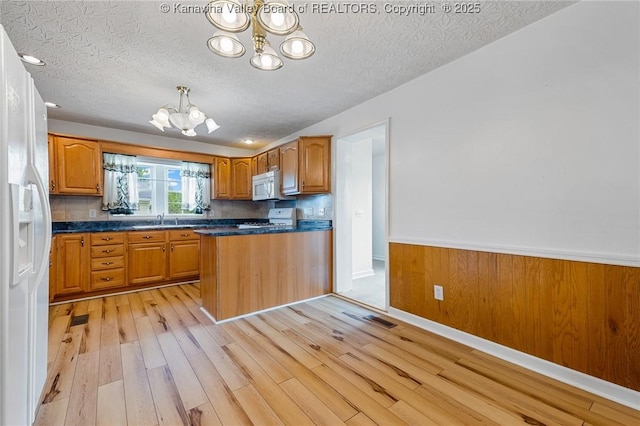 kitchen with a chandelier, white appliances, light wood-style floors, dark countertops, and a textured ceiling