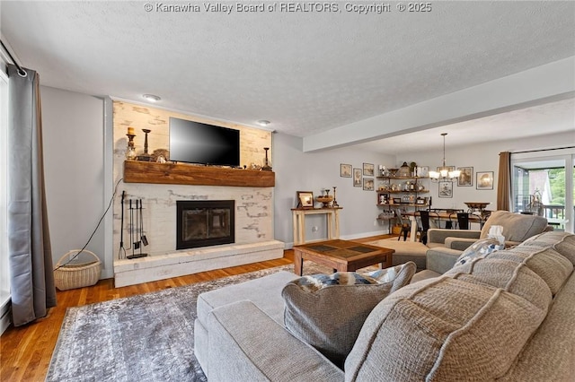 living area with a textured ceiling, a chandelier, a fireplace, light wood-type flooring, and baseboards